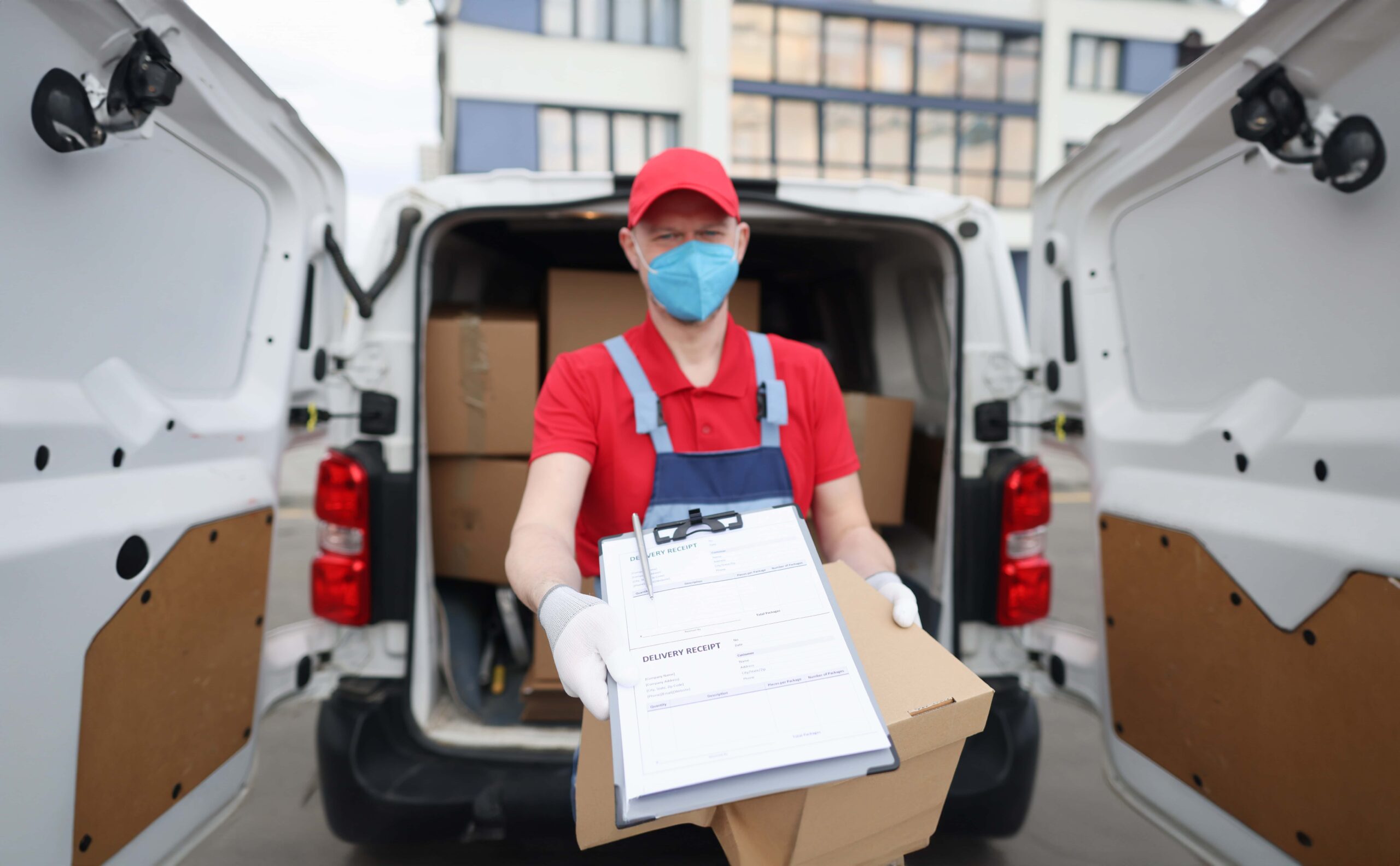 Courier driver in medical protective mask and gloves holds out documents with delivery receipt